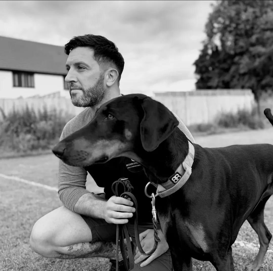 Ryan kneeling beside a Doberman on a playing field, in black and white